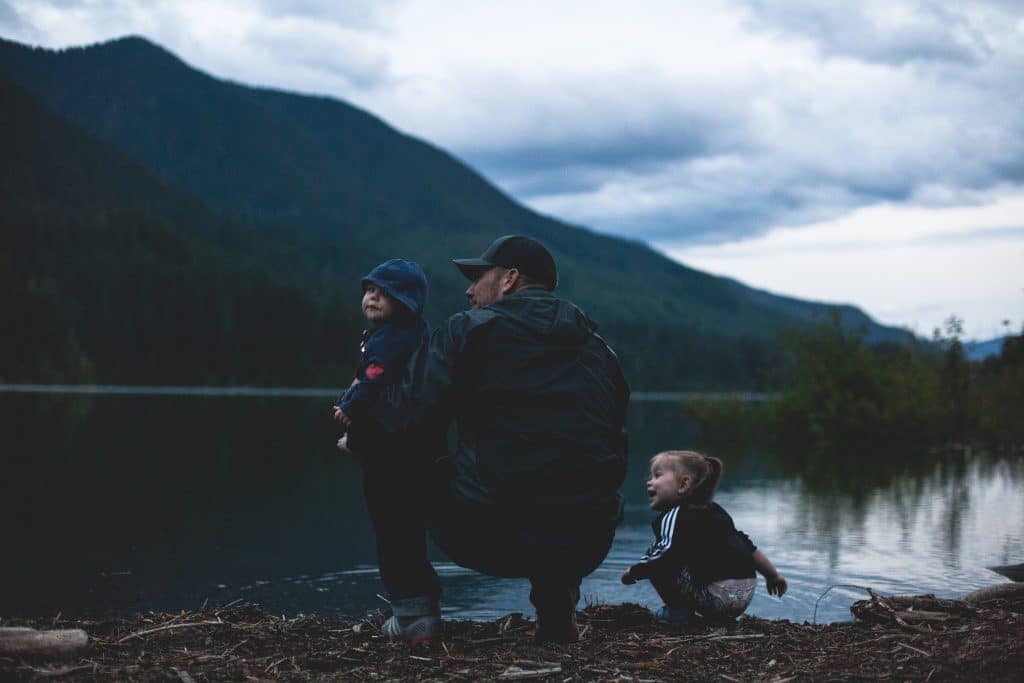 man-with-two-kids-near-body-of-water-1157398 A man with two kids plays near a large lake with forested mountains on the other side, showing the unity of the human and physical environment